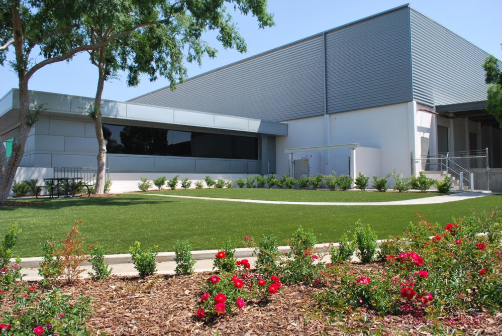 Flowers and artificial turf in front of a large industrial building