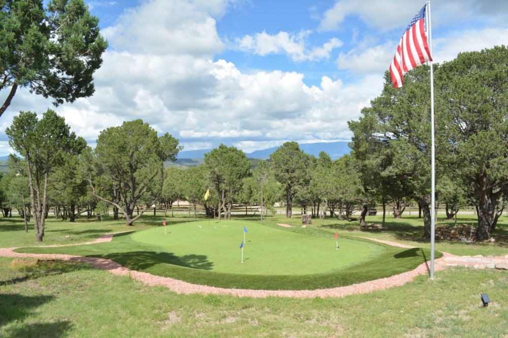 Backyard putting greens set in a natural landscape with multiple flagsticks, smooth artificial turf, and scenic mountain views.