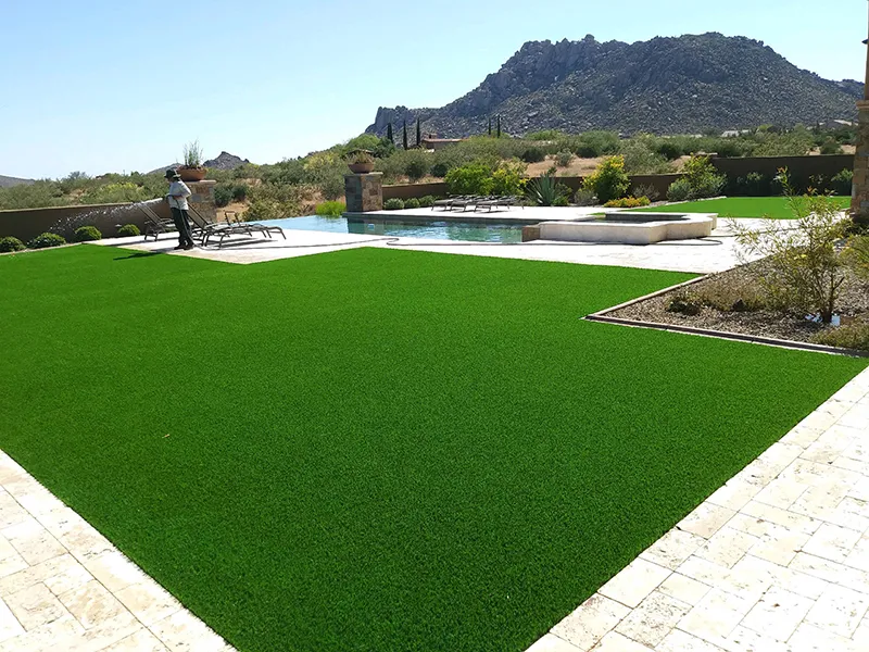 artificial turf in a backyard with a pool and hill in the background