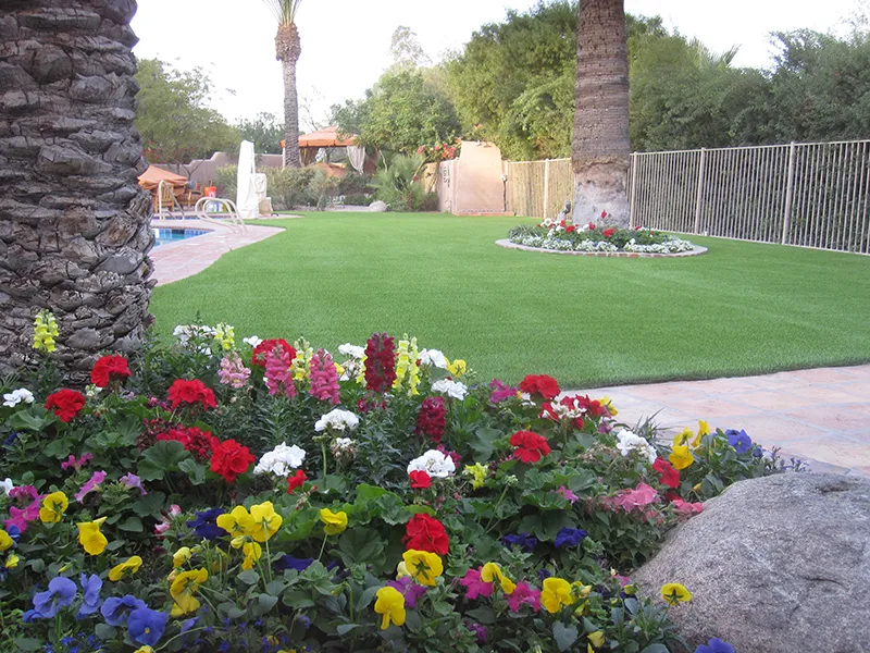 artificial turf in a yard with flowers and a tree