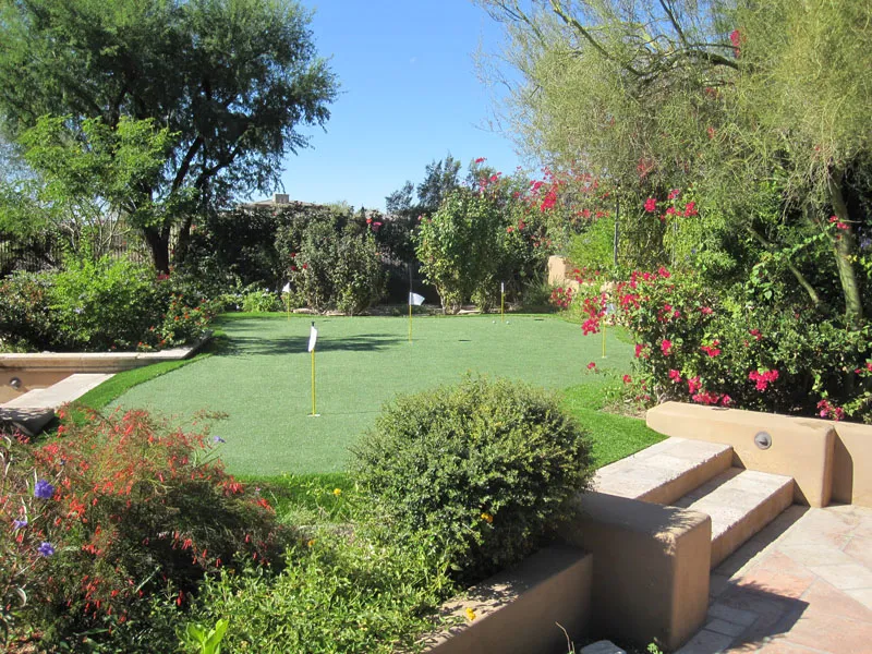 a putting green in a backyard surrounded by flowers