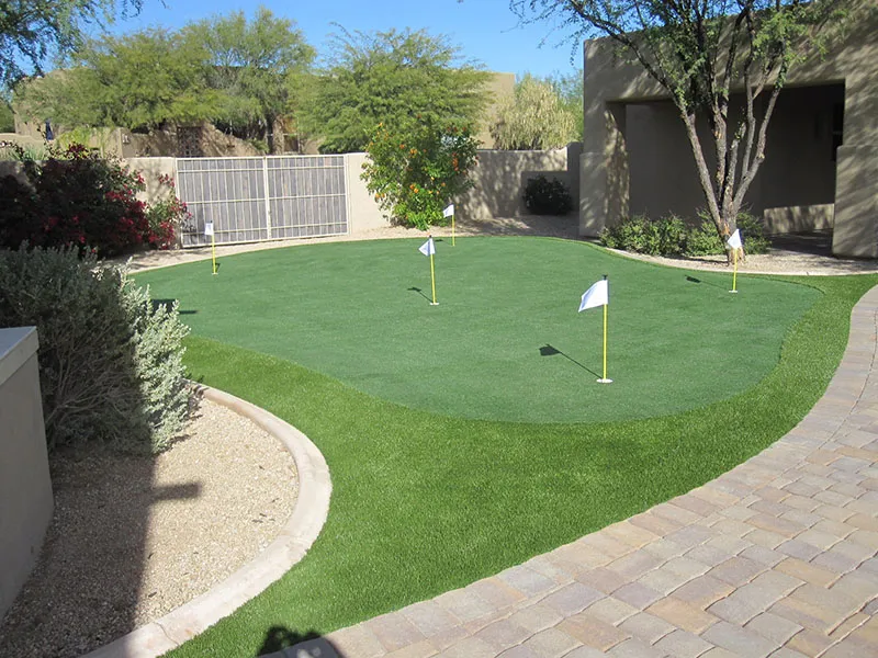 a putting green in a backyard next to a fence and building